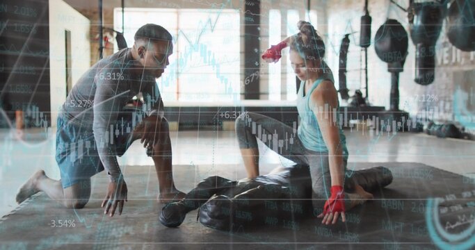 Kneeling trainer guiding client pressing heavy bag in boxing gym with hand wraps, financial charts - Powered by Adobe