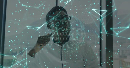 Man wearing glasses holding pen analyzing panel at office desk, with network and dotted globe