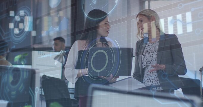 Discussing data two businesswomen in blazers pointing at laptop at office, with digital overlay