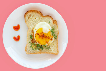 Sandwich with sunny side up egg and fresh thyme on ceramic plate over rose background.
