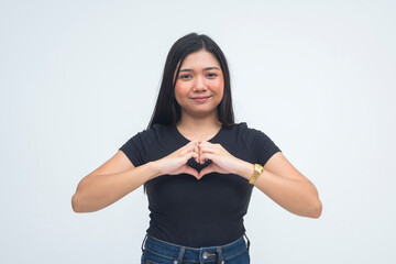 A sweet young Asian woman in a half body shot smiling warmly while making a heart shape with her...