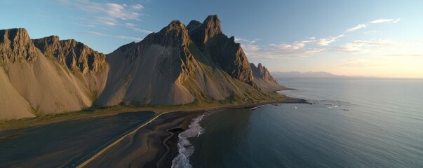 Aerial view of dramatic, rugged mountains meeting the ocean coastline under a bright sky with a sandy beach in the foreground