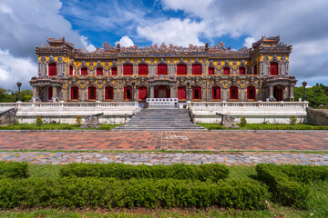 Obraz premium The magnificent, recently restored Kien Trung Palace in Hue, showcasing a vibrant yellow facade, striking red windows, and highly intricate architectural details under a cloudy sky.
