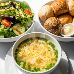 A wholesome meal presentation features a light and flavorful soup, a refreshing salad, and warm, crusty rolls.