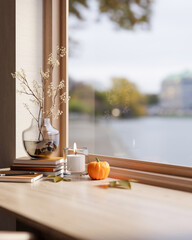 Flowering branch in vase and halloween pumpkin with candles on wooden table aside window in sunlight