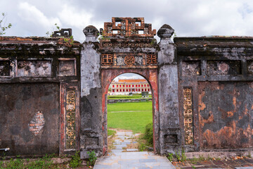 A crumbling, ancient gate in Hue with ornate brickwork frames a distant view of the brightly...
