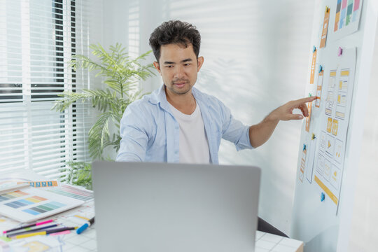 A young designer is working on a UX UI project, analyzing mobile app wireframes and choosing color palettes on a whiteboard. He focuses on brainstorming ideas to improve user experience.