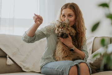 Young beautiful woman with her empty curious cat sitting on the sofa at home