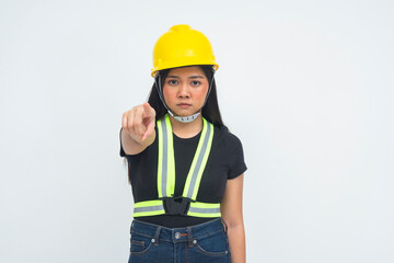 A strict young female engineer in a half body shot wearing a protective helmet, pointing her finger at the camera with a scolding and confrontational expression. Isolated on a white background.