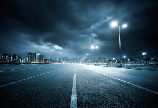 A deserted highway at night under a stormy sky, illuminated by streetlights, leads to distant city buildings - Powered by Adobe