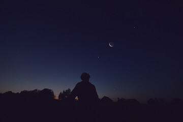 Silhouette of a man observing Moon, Milky Way stars, planets and other celestial objects from a...