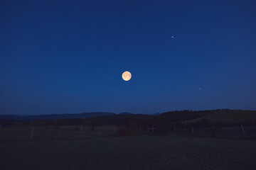 Full Moon with stars, planets and rural countryside tree silhouettes.