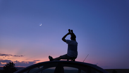Man watching stars, Milky Way, planets, Moon and other celestial objects from a car rooftop from a...