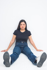 A laid-back young Asian woman in a half body shot sitting on the floor with legs spread, maintaining a neutral and relaxed expression. Isolated on a white background.