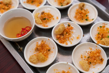 Tiny white bowls hold Beo cake  from Hue, topped with savory ground shrimp and crispy pork rinds, with a small bowl of dipping sauce visible.