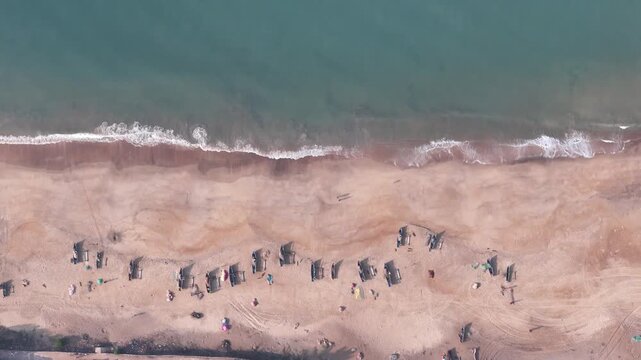 Top-down aerial view of traditional fishing boats arranged in rows on a sandy beach as a wave breaks on the shore in India.