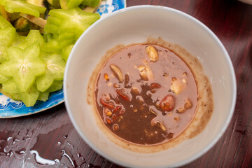 A blue and white plate holds a mix of star fruit slices and green mango with fresh mint leaves, served with a dark dipping sauce on the side.