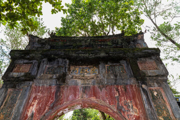 A low-angle close-up shows the weathered, moss-covered archway and decorative lintel of a historic gate at Minh Mang tomb, Hue.