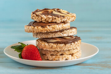 Rice cake with chocolate and nut butter served with fresh strawberry on ceramic plate.
