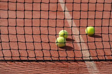 There are three tennis balls positioned behind a net on a tennis court