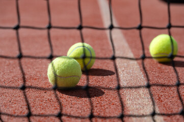 There are three tennis balls located on a tennis court behind a net