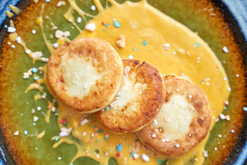 Delicious golden pancakes with cream and colorful sprinkles on green and yellow ceramic plate.