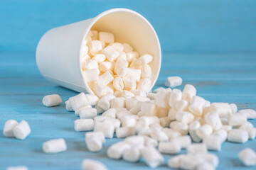 Marshmallows in white paper cup over blue wooden background.