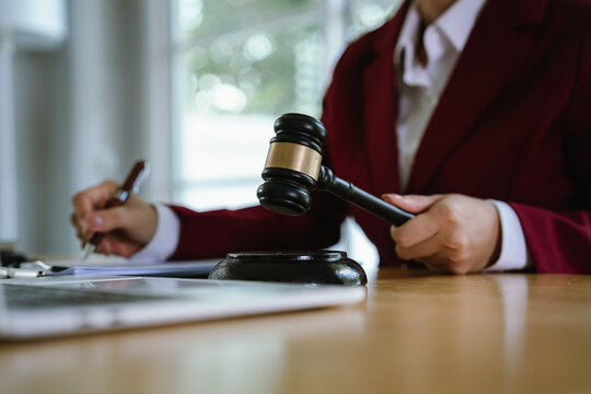 A lawyer carefully reviews and points to a contract document with a pen, beside a laptop, gavel, and justice scales.