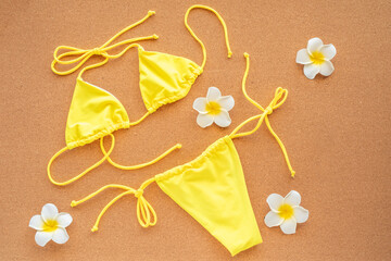 Canary yellow bikini and plumeria flowers on orange background. Summer beach vacation concept. Female swimsuit bikini. Top view.
