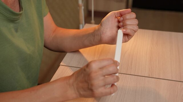 Tight shot of female hands performing a manicure, carefully filing and refining nail edges using a nail file and simple tools. Woman caring for her nails at home