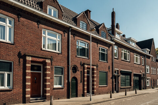 Brick houses feature large windows and distinct architectural styles, creating an inviting urban atmosphere with warm sunlight. Eindhoven in the Netherlands