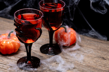 Halloween spooky red cocktail in skeleton hand glass on wooden table and dark background