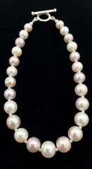 A delicate pearl necklace features lustrous, round pearls in a variety of creamy white and light pink hues.