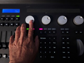 A person operating a professional lighting console panel with one hand, adjusting control knobs and buttons in a studio or live event setting.