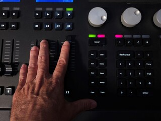 A person operating a professional lighting console panel with one hand, adjusting buttons in a studio or live event setting.
