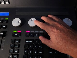 A person operating a professional lighting console panel with one hand, adjusting control knobs and buttons in a studio or live event setting.