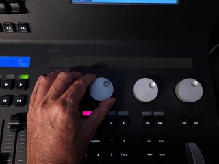A person operating a professional lighting console panel with one hand, adjusting control knobs and buttons in a studio or live event setting.