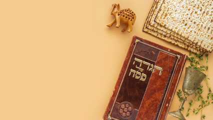 Jewish holiday Pesach celebration concept. Traditional book with text in Hebrew: "Passover Haggadah" ("Passover Tale"), Kiddush cup, matzah on beige background.
