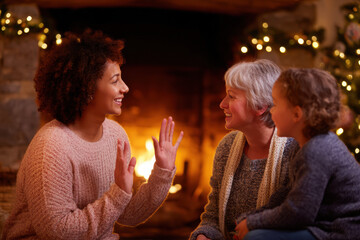 Happy multi generational family uses sign language for communication, sharing story. Mother, grandmother, and child sit by cozy fireplace, feeling love and togetherness