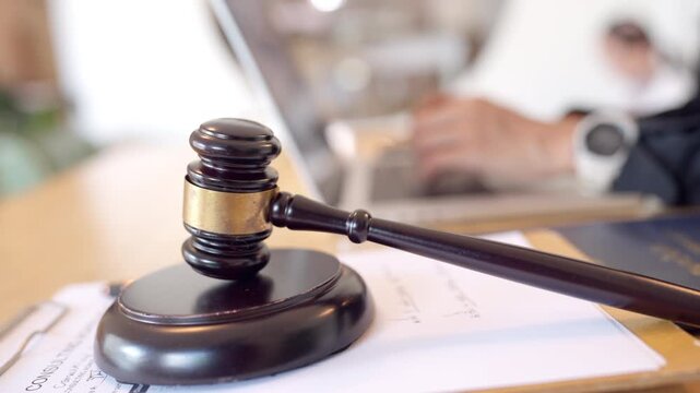 Close up of a judge gavel on a legal document with a female lawyer working in the background. Symbol of authority in digital legal services.