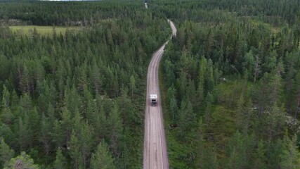 Aerial view of a vehicle driving down a winding, unpaved road through a dense forest in Sweden