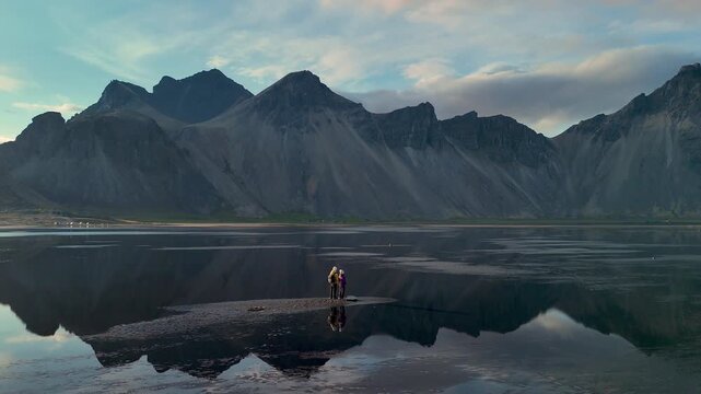Explore the breathtaking vistas of Iceland where adventurers stand on the shore, surrounded by majestic mountains reflecting in tranquil waters during a soft twilight. Natures beauty is unmatched.
