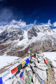 Vertical View of Prayer Flags and Stone Cairn on Snow-Draped Kyanjin Ri Summit Overlooking Langtang Glacier and Himalayan Peaks
