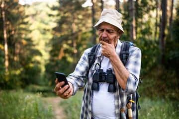 Upset senior hiker got lost and he is using smartphone to find right direction while hiking in the nature.	