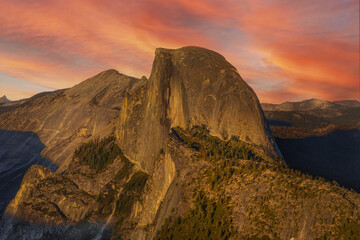 Magnificent Half Dome mountain in Yosemite National Park, California, under a glowing orange sunset sky, showcasing dramatic granite cliffs and breathtaking wilderness landscape for travel concepts.