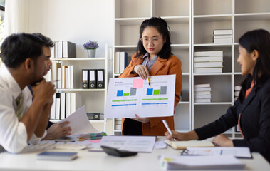 Asian businesswoman explaining and showing growth chart to colleagues during office meeting.