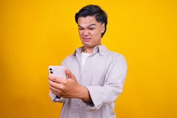Young Asian Man Reacting With Disgust To Something On Smartphone Isolated On Yellow Background