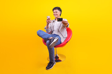 Cheerful Young Asian Man Using Mobile Phone And Holding Credit Card For Online Shopping