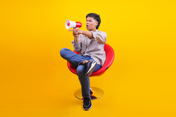 Excited Young Asian Man Announces News With Megaphone While Seated In Red Chair