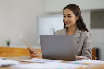Businesswoman working with financial documents on laptop in office.